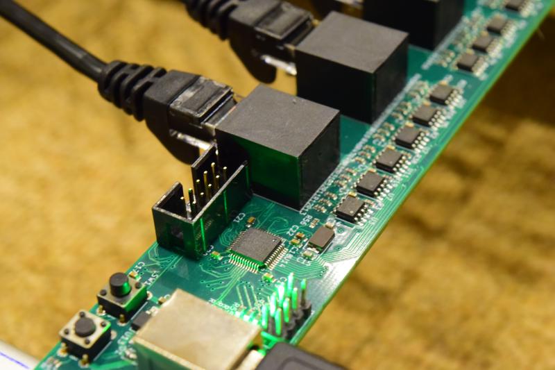 Close up of a narrow board with a bunch of small ICs next to RJ-45 connectorsm as well as a microcontroller IC